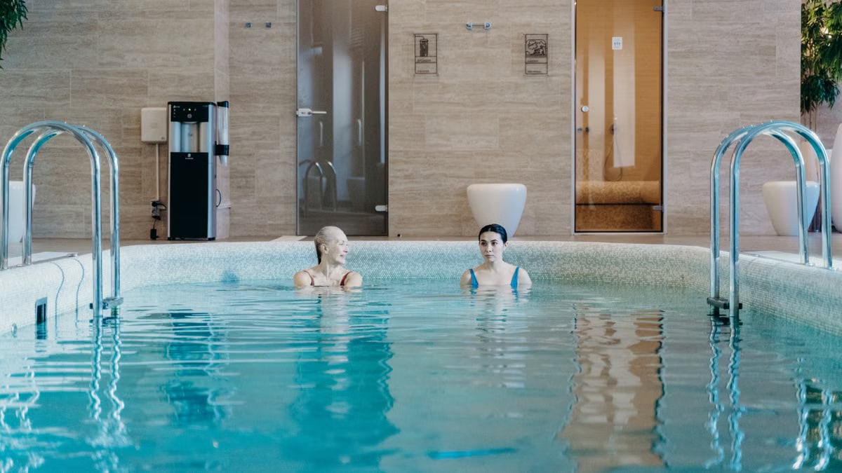Two women enjoying a leisurely swim in an indoor pool, capturing relaxation and tranquility.